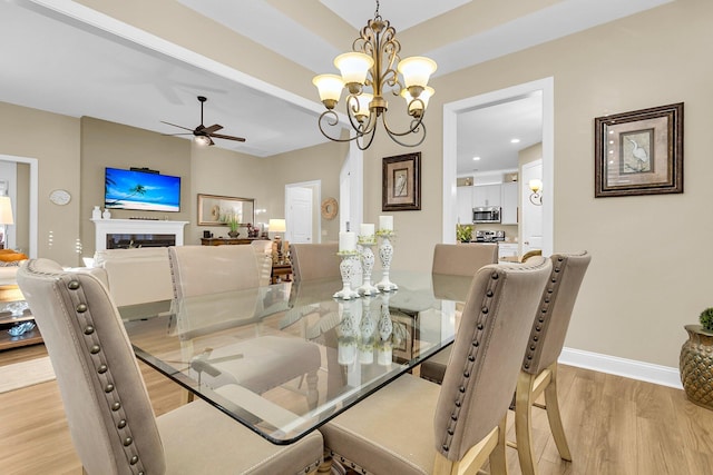 dining room with ceiling fan with notable chandelier and light hardwood / wood-style floors