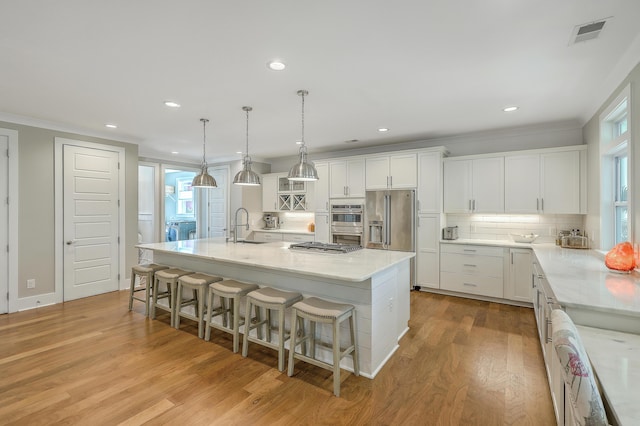 kitchen with stainless steel appliances, a center island with sink, tasteful backsplash, a kitchen bar, and white cabinets