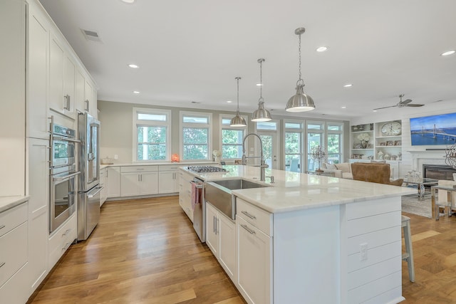 kitchen featuring a center island with sink, pendant lighting, a fireplace, white cabinetry, and built in features