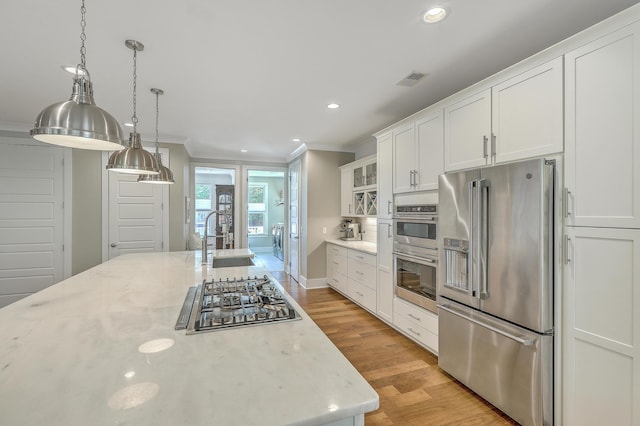 kitchen featuring light stone countertops, light wood-type flooring, white cabinetry, appliances with stainless steel finishes, and sink