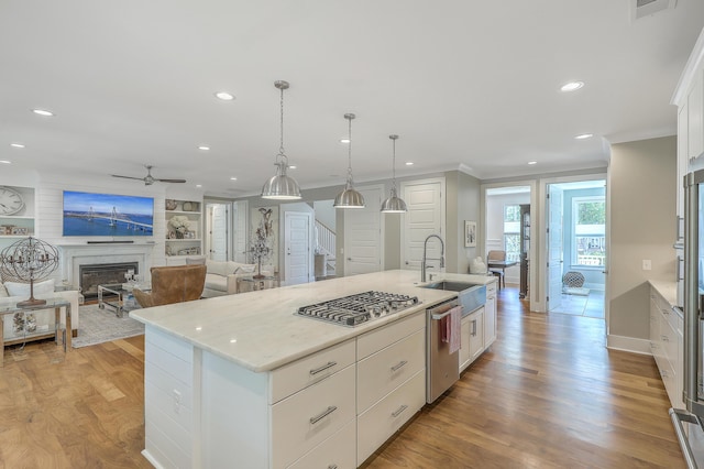 kitchen featuring a center island with sink, stainless steel appliances, pendant lighting, a fireplace, and white cabinetry