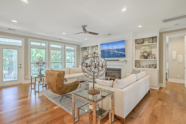 living room featuring ornamental molding, ceiling fan, built in features, light hardwood / wood-style flooring, and a high end fireplace