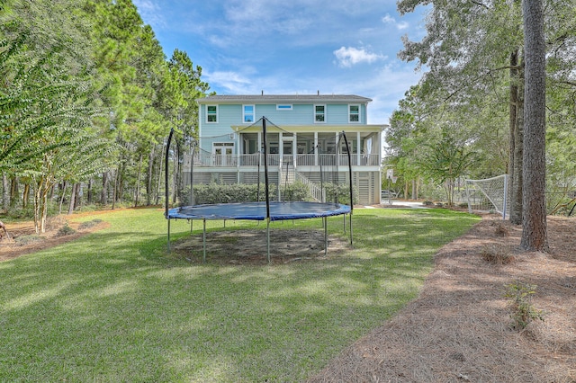 rear view of house with a lawn, a sunroom, and a trampoline