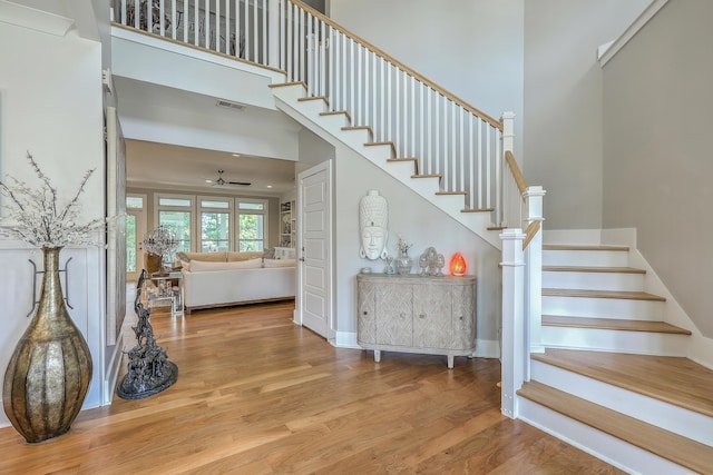 staircase featuring a towering ceiling, wood-type flooring, and ceiling fan