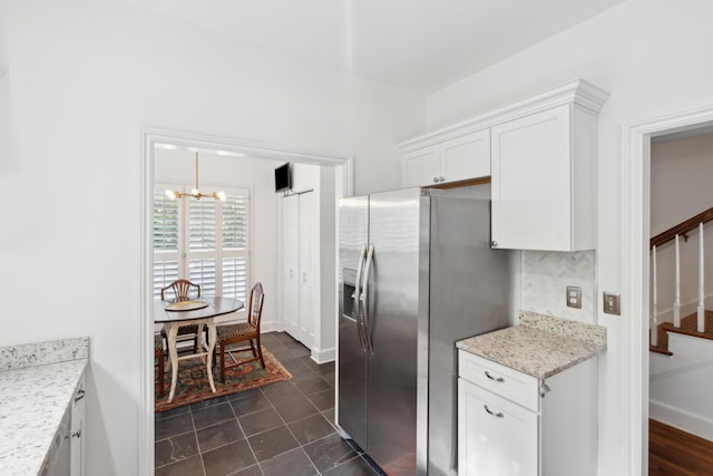 kitchen featuring light stone countertops, stainless steel fridge with ice dispenser, white cabinets, baseboards, and a notable chandelier