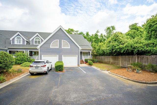 exterior space featuring a garage, aphalt driveway, fence, and a shingled roof