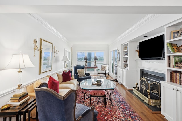 living room featuring built in shelves, a fireplace with raised hearth, ornamental molding, and wood finished floors