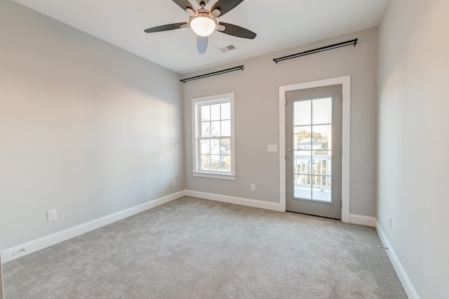 empty room featuring visible vents, light carpet, baseboards, and a ceiling fan