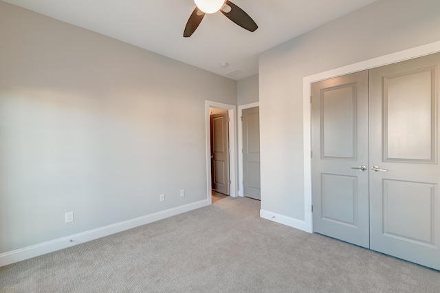 unfurnished bedroom featuring a closet, baseboards, light colored carpet, and a ceiling fan