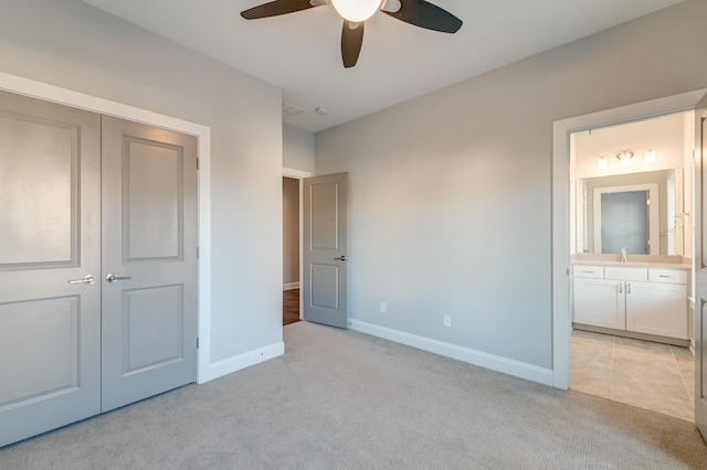 unfurnished bedroom featuring light carpet, a sink, ensuite bath, a closet, and baseboards