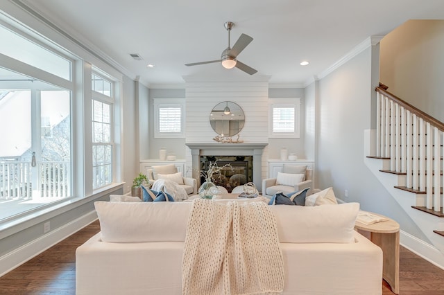 living area with dark wood finished floors, visible vents, a glass covered fireplace, and ornamental molding