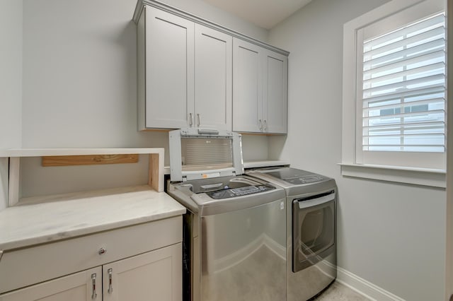 clothes washing area featuring baseboards, cabinet space, and washing machine and dryer