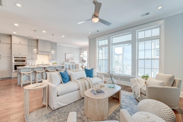 living area with visible vents, ornamental molding, and light wood-style flooring