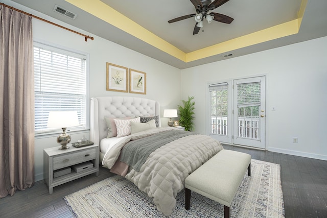 bedroom featuring ceiling fan, dark hardwood / wood-style flooring, a raised ceiling, and access to outside