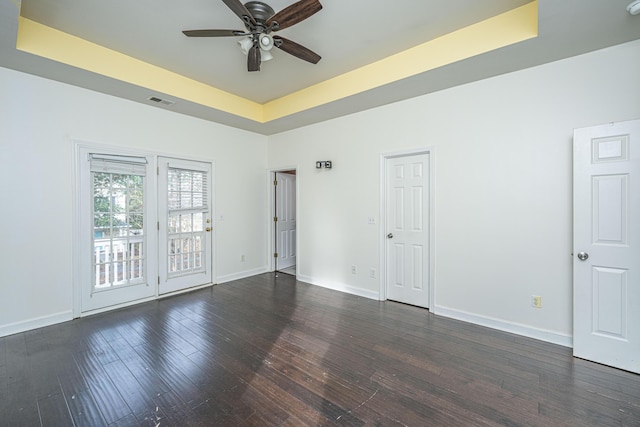 empty room featuring a raised ceiling, ceiling fan, and dark hardwood / wood-style floors