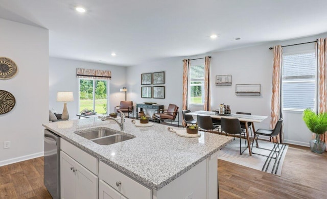 kitchen with sink, hardwood / wood-style flooring, white cabinetry, light stone countertops, and a center island with sink