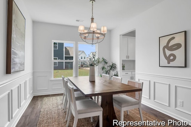 dining room with visible vents, dark wood-type flooring, a chandelier, wainscoting, and a decorative wall