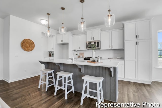 kitchen featuring white cabinetry, stainless steel microwave, dark wood-style floors, and light countertops