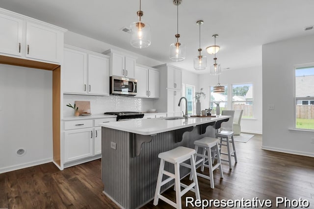 kitchen with visible vents, a center island with sink, white cabinets, stainless steel appliances, and a sink