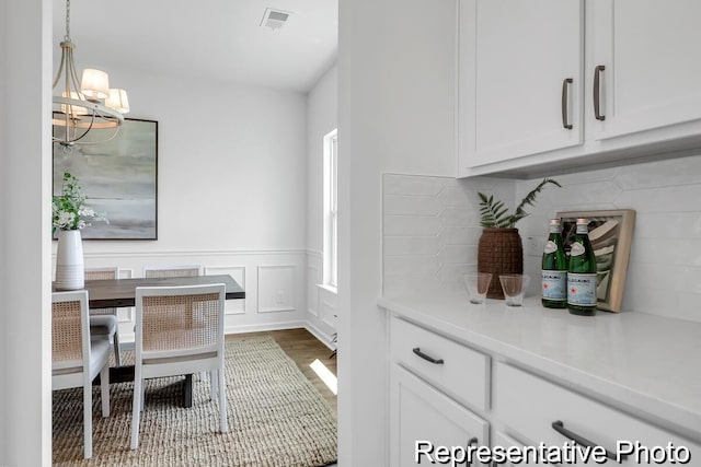 home office with visible vents, a wainscoted wall, a notable chandelier, wood finished floors, and a decorative wall