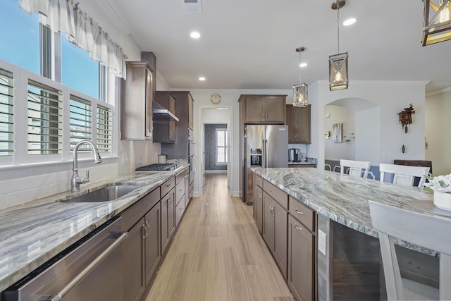 kitchen featuring light wood finished floors, beverage cooler, arched walkways, appliances with stainless steel finishes, and a sink