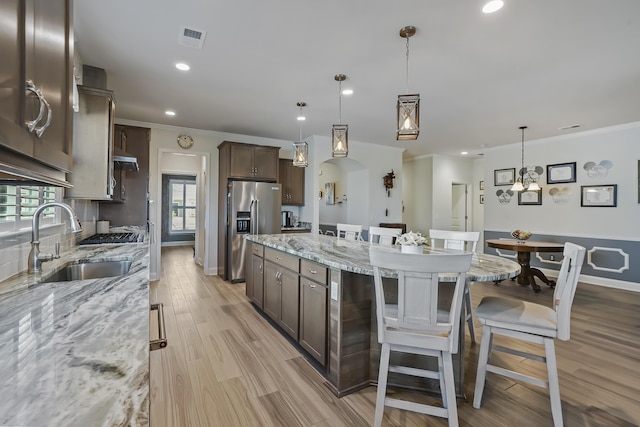 kitchen with a sink, visible vents, a kitchen breakfast bar, dark brown cabinets, and stainless steel refrigerator with ice dispenser