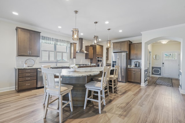 kitchen with arched walkways, stainless steel appliances, light wood-style floors, a kitchen island, and wall chimney exhaust hood