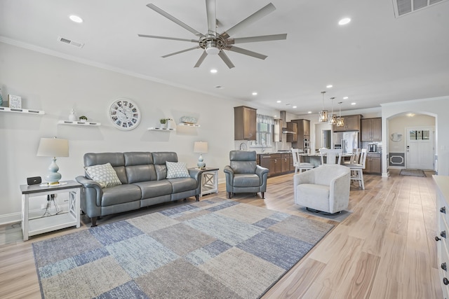 living area featuring light wood-type flooring, arched walkways, visible vents, and ornamental molding