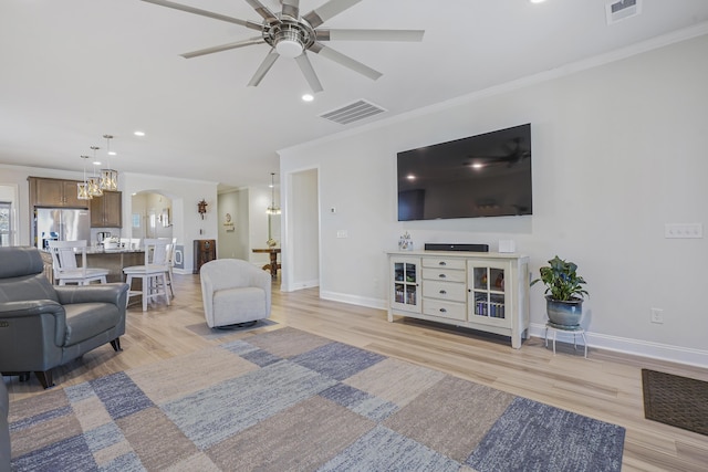 living area with light wood-type flooring, baseboards, visible vents, and ornamental molding