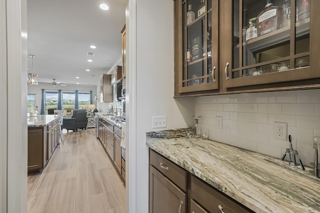 kitchen with light wood finished floors, glass insert cabinets, open floor plan, light stone countertops, and backsplash