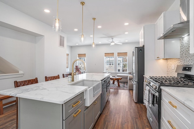 kitchen featuring a kitchen bar, tasteful backsplash, appliances with stainless steel finishes, a kitchen island with sink, and wall chimney range hood