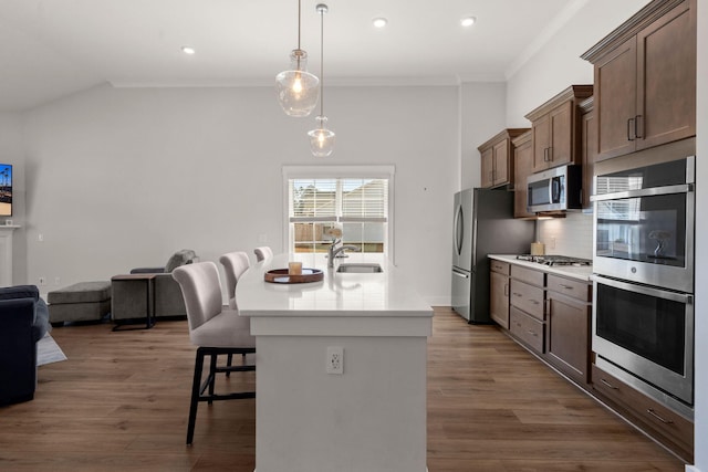 kitchen with a breakfast bar, light countertops, backsplash, appliances with stainless steel finishes, and a kitchen island with sink