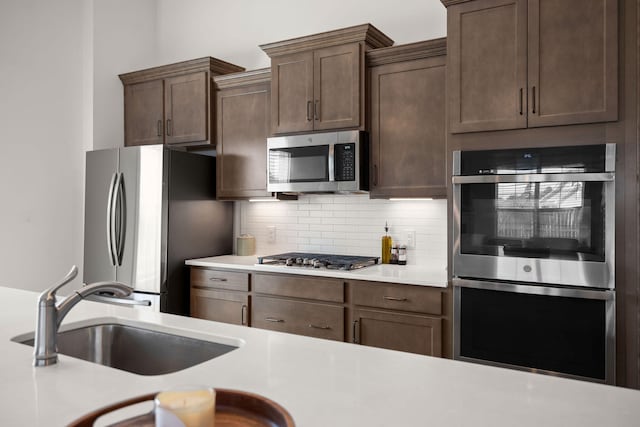 kitchen featuring dark brown cabinetry, decorative backsplash, stainless steel appliances, light countertops, and a sink