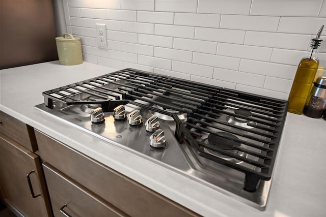 room details featuring light countertops, stainless steel gas cooktop, decorative backsplash, and dark brown cabinets