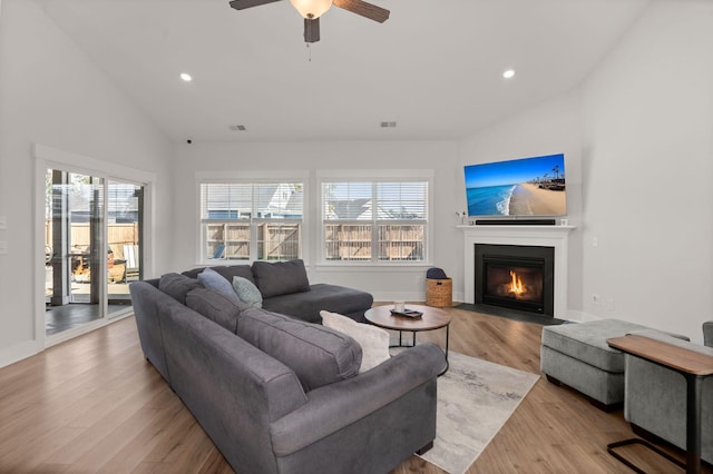 living area with lofted ceiling, recessed lighting, a fireplace with flush hearth, visible vents, and wood finished floors