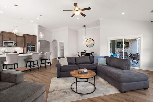 living room with arched walkways, light wood-type flooring, a ceiling fan, and crown molding