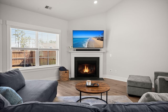 living area featuring vaulted ceiling, wood finished floors, visible vents, and baseboards