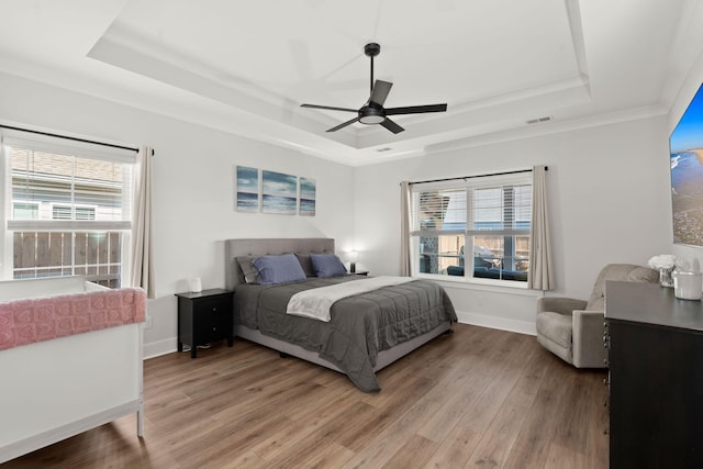 bedroom featuring a tray ceiling, baseboards, visible vents, and light wood finished floors