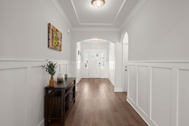 foyer featuring arched walkways, wainscoting, dark wood-type flooring, crown molding, and a decorative wall