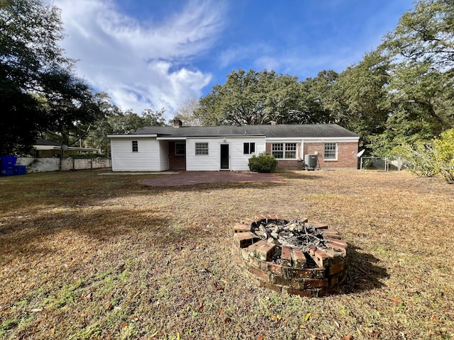 back of property with an outdoor fire pit, fence, a lawn, brick siding, and a patio area