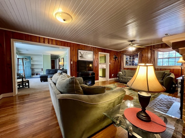 living area featuring wood walls, wood finished floors, built in features, crown molding, and a ceiling fan