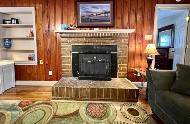 living room with light wood finished floors, wood walls, a brick fireplace, and built in features