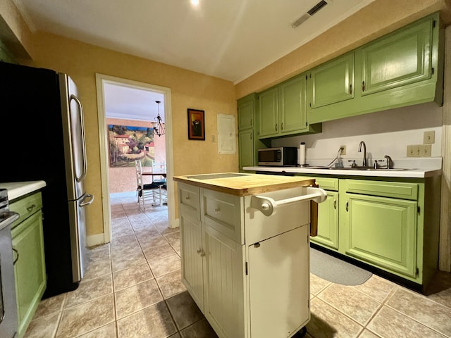 kitchen with a sink, stainless steel appliances, green cabinetry, light tile patterned flooring, and a center island