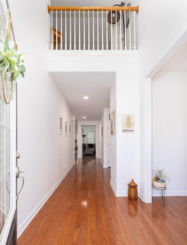 hallway with a high ceiling, wood finished floors, baseboards, and recessed lighting
