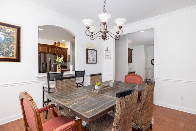 dining area with baseboards, arched walkways, an inviting chandelier, hardwood / wood-style flooring, and crown molding