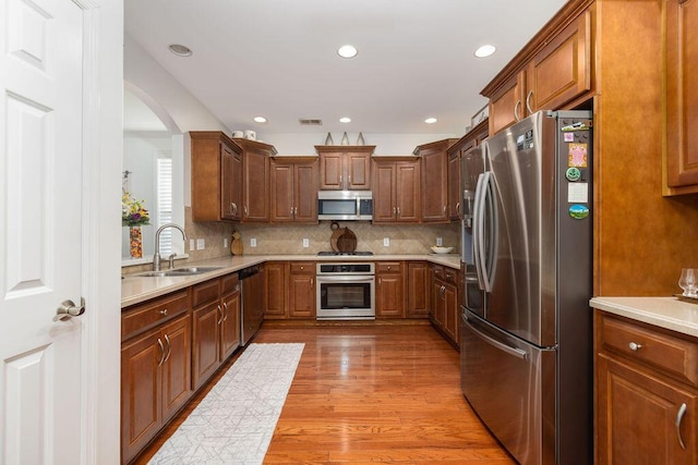 kitchen featuring tasteful backsplash, a sink, light countertops, light wood-type flooring, and stainless steel appliances