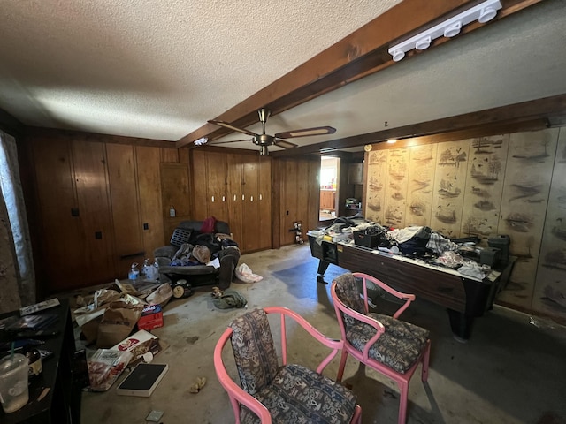 interior space with a ceiling fan, a textured ceiling, wood walls, and unfinished concrete floors