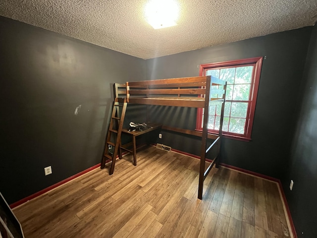 unfurnished bedroom with visible vents, baseboards, a textured ceiling, and wood finished floors