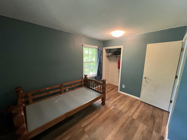 bedroom with baseboards, a closet, a textured ceiling, and wood finished floors