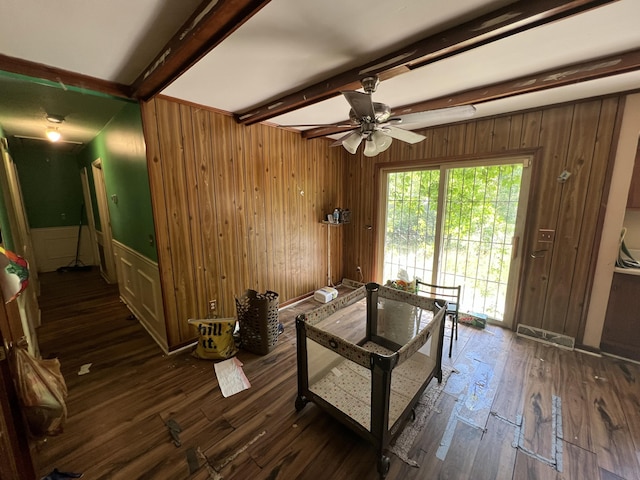 dining room with wooden walls, ceiling fan, beamed ceiling, and dark wood-style floors